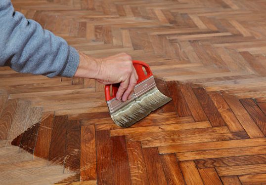 Varnishing of oak parquet floor, workers hand and brush